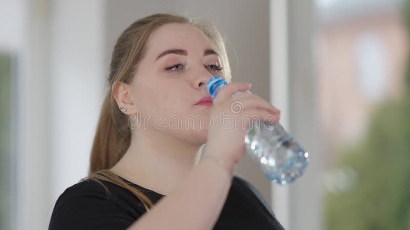 Nahaufnahme Gesicht von erschöpften plumpen Sportlerin trinken erfrischendes Wasser nach dem Training in Innenräumen. Porträt der