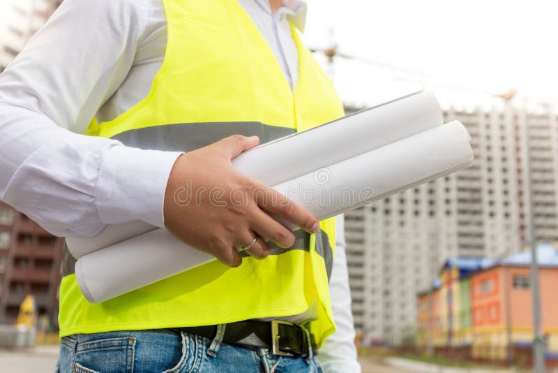 Nahaufnahmebild des Ingenieurs in der Sicherheitswestenholding rollte blueprin stockbild Nahaufnahmebild des Ingenieurs in der Sicherheitswestenholding rollte blueprin stockbild