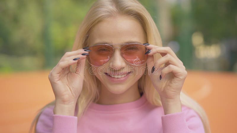 Nahaufnahmegesicht der hübschen blonden Frau, die eine Sonnenbrille festlegt und an der Kamera blinzelt. Porträt des glamourösen K stock video