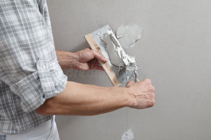Nahaufnahmehandmanntrockenmauerarbeitskraft oder -Gipser, die auf Stuck Gipskartonwand mithilfe einer Kelle und einer Spachtel, di stockbild