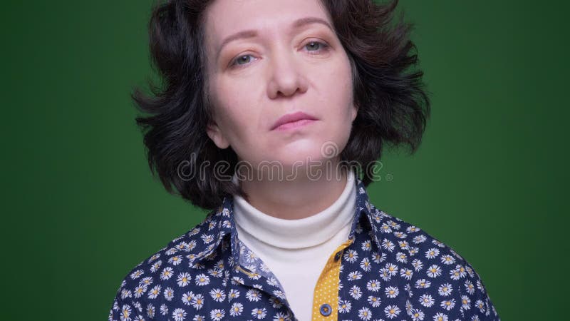 Nahaufnahmeporträt der älteren kaukasischen brunette Frau, die gerade Kamera mit dem Hintergrund lokalisiert auf Grün betrachtet