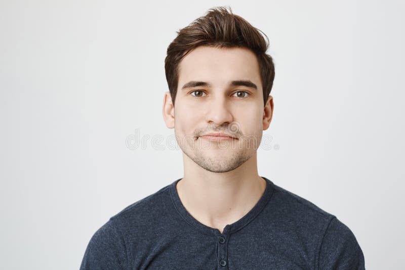 Nahaufnahmeporträt des netten europäischen Kerls mit stilvollem Haarschnitt und curvy Lächeln, stehend gegen grauen Hintergrund k stockbild