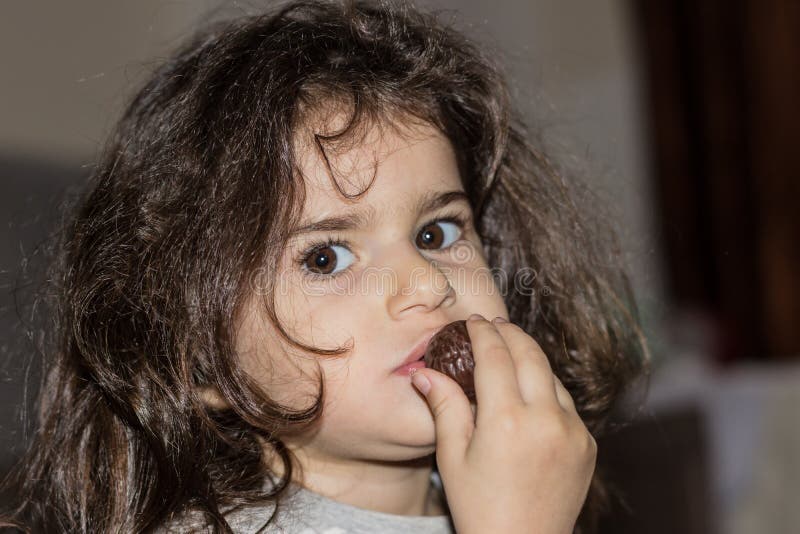 Nahaufnahmeportr?t eines kleinen M?dchens mit dem gelockten Haar Das Kind isst Praline lizenzfreie stockfotos Nahaufnahmeportr?t eines kleinen M?dchens mit dem gelockten Haar Das Kind isst Praline lizenzfreie stockfotos