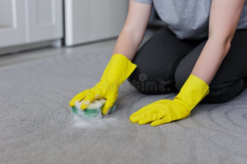 Nahe der weiblichen Hände in gelben Gummihandschuhen reinigen Teppich mit Schwamm und Schaum
