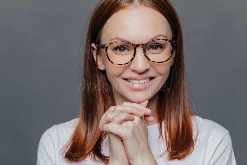 Naher hoher Schuss der glücklichen jungen europäischen Frau hat angenehmes Lächeln, hält Hände zusammen nahe Kinn, trägt zufällig lizenzfreie stockbilder Naher hoher Schuss der glücklichen jungen europäischen Frau hat angenehmes Lächeln, hält Hände zusammen nahe Kinn, trägt zufällig lizenzfreie stockbilder