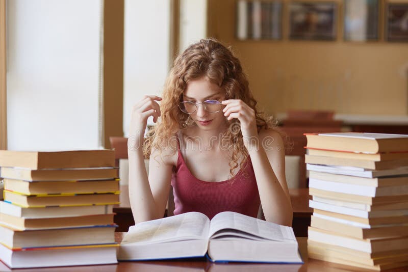 Nahes hohes Porträt der jungen Frau ihre Brillen berührend, Papierbuch lesend Studentinausgabenüberstunden, tragende Gläser stockfotografie Nahes hohes Porträt der jungen Frau ihre Brillen berührend, Papierbuch lesend Studentinausgabenüberstunden, tragende Gläser stockfotografie