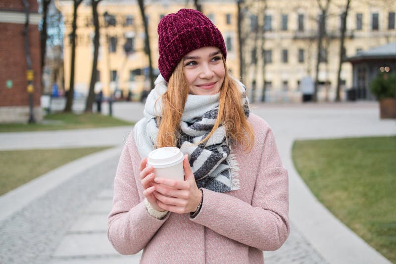 Nahes hohes Porträt des jungen stilvollen blonden Mädchens im roten Hut, der zum Mitnehmen Kaffeetasse hält lizenzfreies stockfoto Nahes hohes Porträt des jungen stilvollen blonden Mädchens im roten Hut, der zum Mitnehmen Kaffeetasse hält lizenzfreies stockfoto