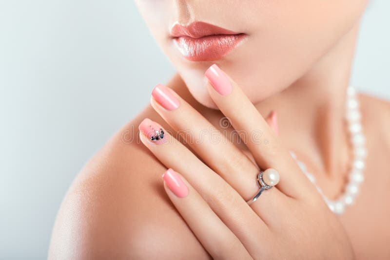 Nail art and design. Beautiful woman wearing make-up and pearl jewellery showing pink manicure with gems stock photography Nail art and design. Beautiful woman wearing make-up and pearl jewellery showing pink manicure with gems stock photography