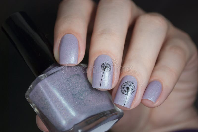 Nail polish in a hand on a black background. Gentle nail art with dandelions.