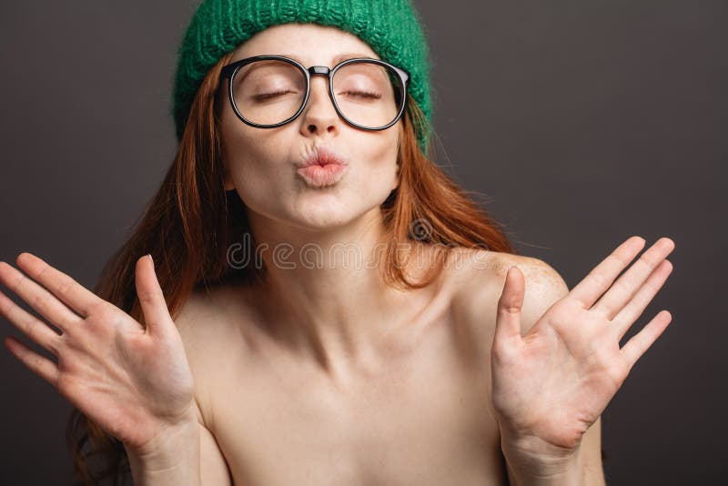 Ginger woman wearing glasses and green hat pouting her lips ready for kiss....