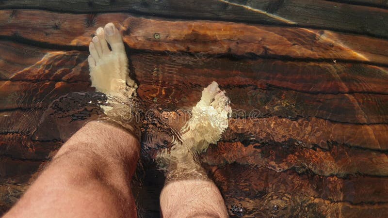 Naked hairy male legs walk on pier. The legs of a man swim. First person of view. Men rest on a flood wood underwater pier. The pavement is covered with water in the lake.