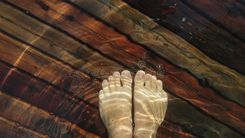 Naked hairy male legs walk on pier. The legs of a man swim. First person of view. Men rest on a flood wood underwater pier. The pavement is covered with water in the lake.