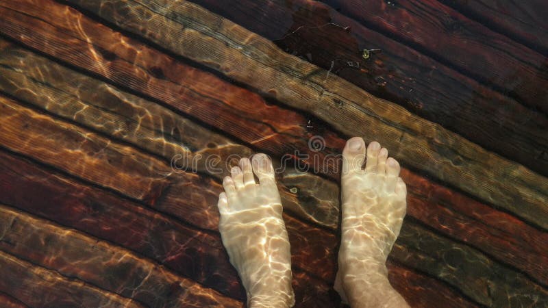 Naked hairy male legs walk on pier. The legs of a man swim. First person of view. Men rest on a flood wood underwater pier. The pavement is covered with water in the lake.
