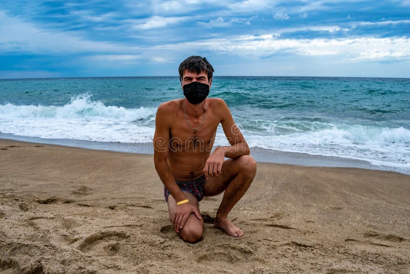 Naked Man in Swimming Trunks and a Medical Protective Mask on the Beach Against the Background of the Blue-turquoise image