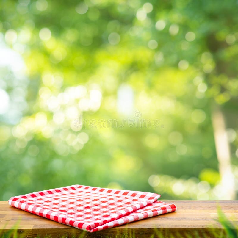 Red checked tablecloth on wood with blur green bokeh of tree background.Summer and picnic concepts.Design for key visual food and drink products.no people. Red checked tablecloth on wood with blur green bokeh of tree background.Summer and picnic concepts.Design for key visual food and drink products.no people