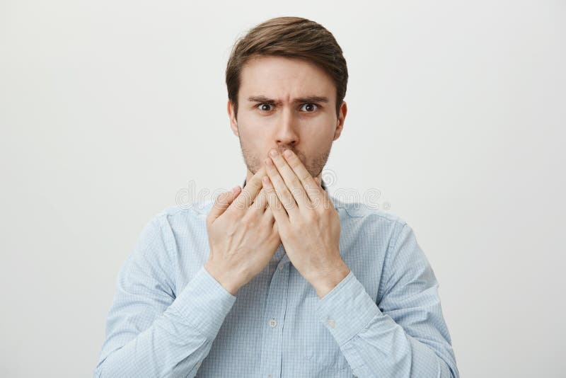 Did I really said that. Portrait of attractive young caucasian male expressing regret of revealing secret, covering mouth with crossed palms and frowning with shock, standing over gray background. Copy space. Did I really said that. Portrait of attractive young caucasian male expressing regret of revealing secret, covering mouth with crossed palms and frowning with shock, standing over gray background. Copy space