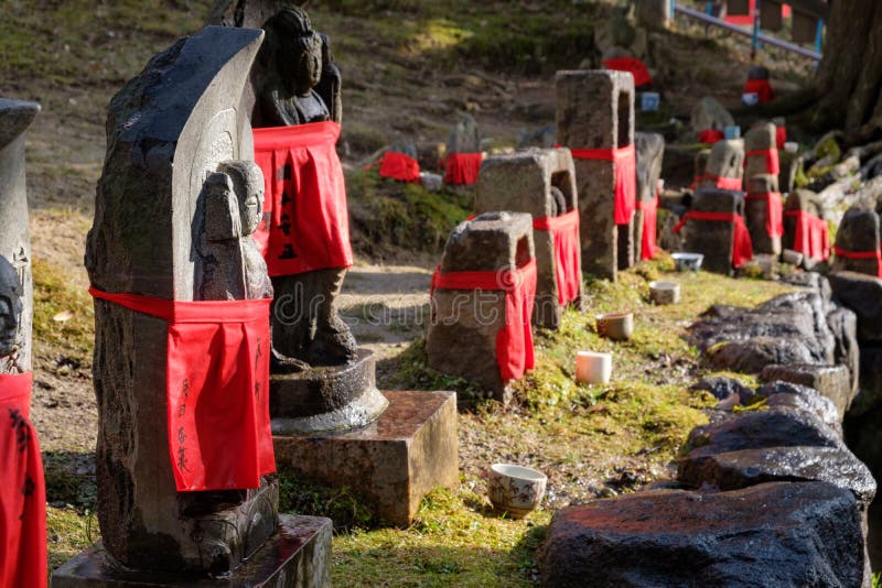 NARA, JAPÃO - 30 DE JANEIRO DE 2018: Esculturas de pedra da Buda que vestem a roupa vermelha no templo de Nara do lado imagem de stock NARA, JAPÃO - 30 DE JANEIRO DE 2018: Esculturas de pedra da Buda que vestem a roupa vermelha no templo de Nara do lado imagem de stock