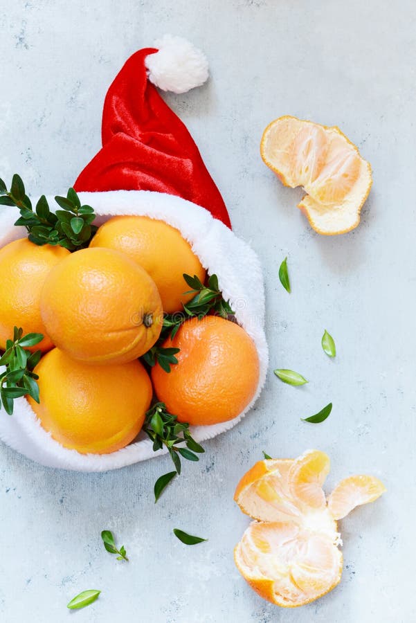 Naranjas maduras en el sombrero de Santa Claus con la planta del boj en un fondo azul Humor festivo imagen de archivo libre de regalías Naranjas maduras en el sombrero de Santa Claus con la planta del boj en un fondo azul Humor festivo imagen de archivo libre de regalías