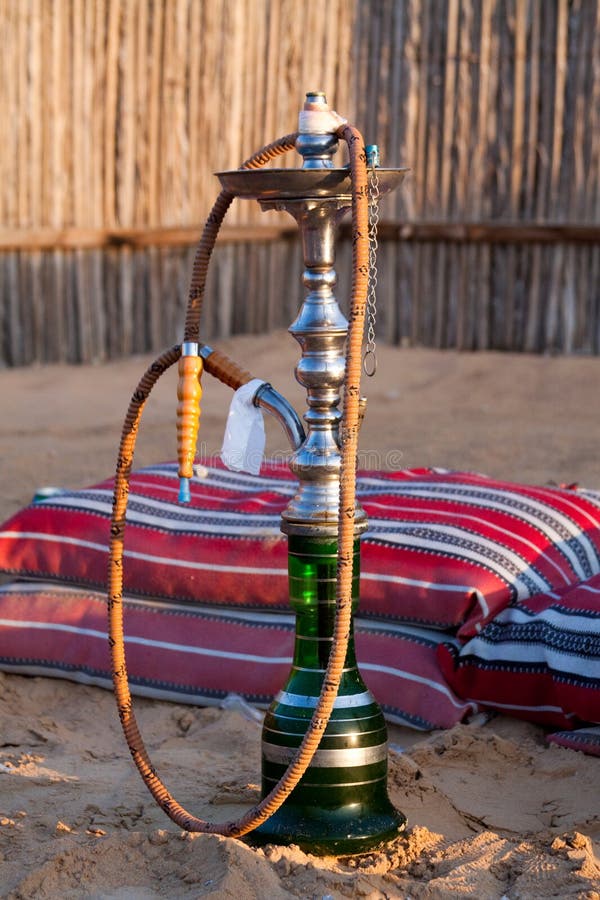Shot taken during a safari in the desert near Dubai, UAE. Picture is of a hookah / shisha water pipe in the sand next to Arabic pillow cushions at sunrise. Shot taken during a safari in the desert near Dubai, UAE. Picture is of a hookah / shisha water pipe in the sand next to Arabic pillow cushions at sunrise.