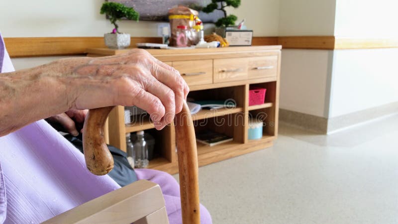 Narrabri, NSW/Australia - 12/03/2017: Elderly woman sitting down in nursing home holding her walking stick. Side on view, hand and cane only in frame with background of room.