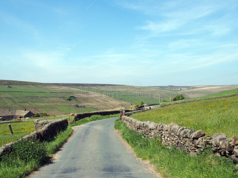 Narrow country lane surrounded by dy stone walls in a sunlit rural hilly landscape on the old howarth road in calderdale west