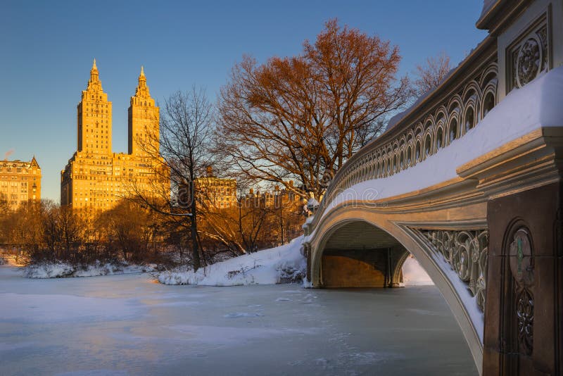 Cold Central Park winter sunrise on the frozen Lake with the Bow Bridge and Upper West Side buildings. Wintertime in Manhattan, New York City. Cold Central Park winter sunrise on the frozen Lake with the Bow Bridge and Upper West Side buildings. Wintertime in Manhattan, New York City