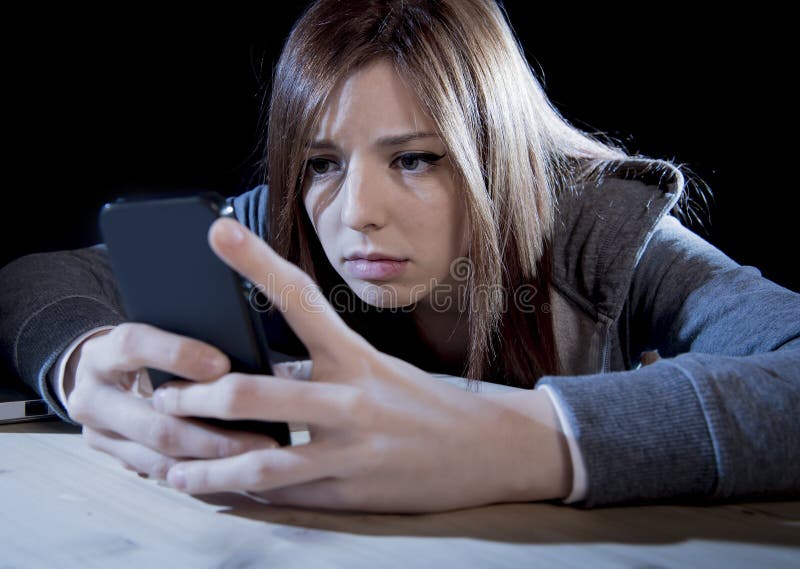 Nastolatek dziewczyna patrzeje martwiący się i desperacki telefon komórkowy gdy internet podkradał się ofiara nadużywającego cybe