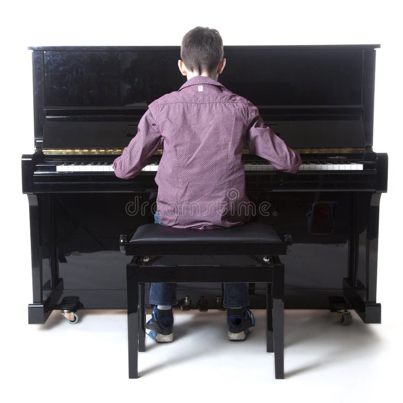 Nastoletni chłopak siedzi przy pionowym pianinem w studiu