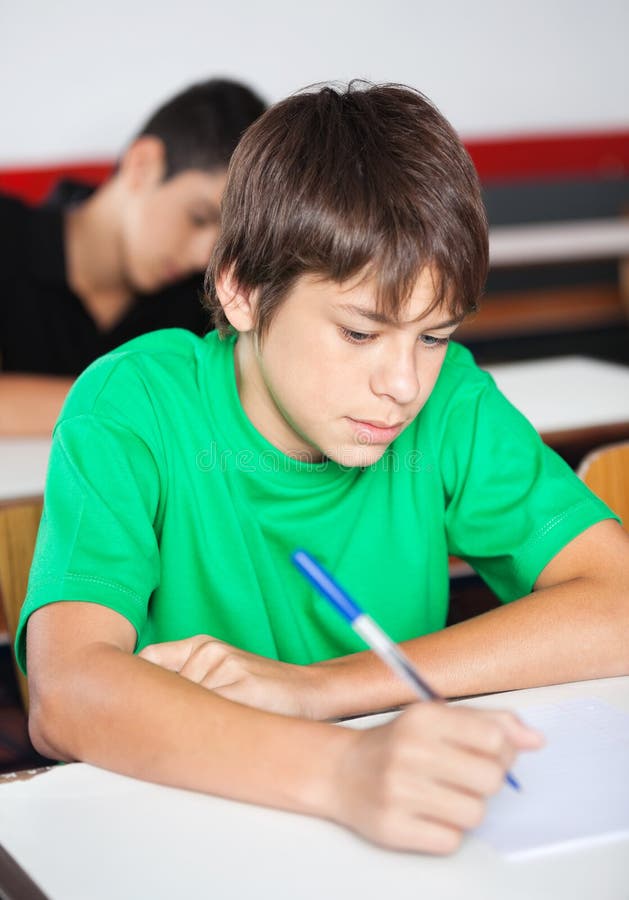 Nastoletni Uczniowski Writing Przy biurkiem Podczas fotografia stock Nastoletni Uczniowski Writing Przy biurkiem Podczas fotografia stock