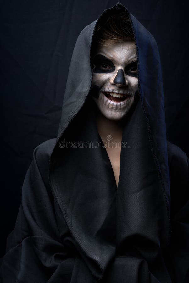 Teen with make-up of the skull in a black cloak laughs. Teen with make-up of the skull in a black cloak laughs