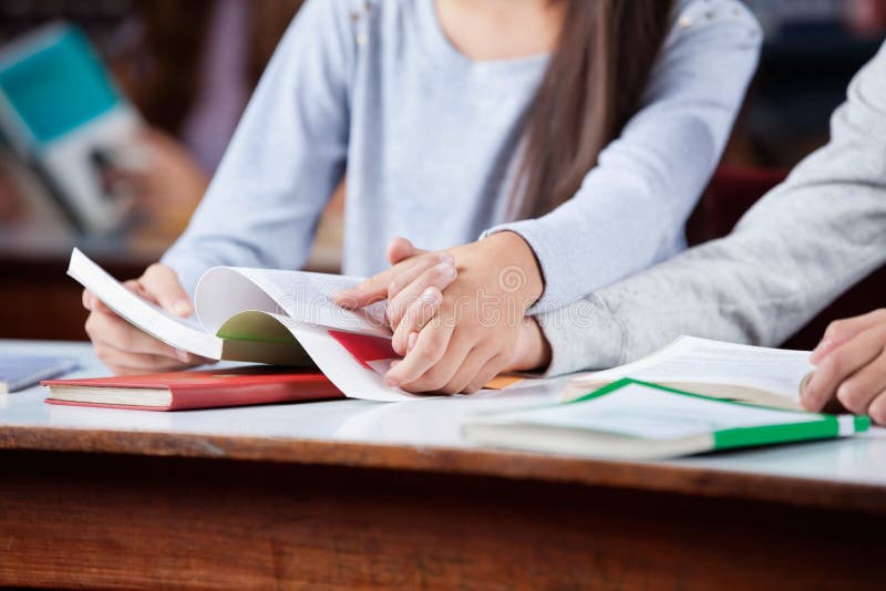 Nastoletnie pary mienia ręki Przy stołem W bibliotece obraz stock Nastoletnie pary mienia ręki Przy stołem W bibliotece obraz stock