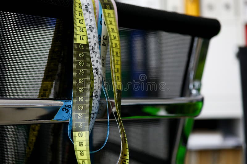 Nastri di misurazione che appendono su una sedia nera immagine stock Nastri di misurazione che appendono su una sedia nera immagine stock