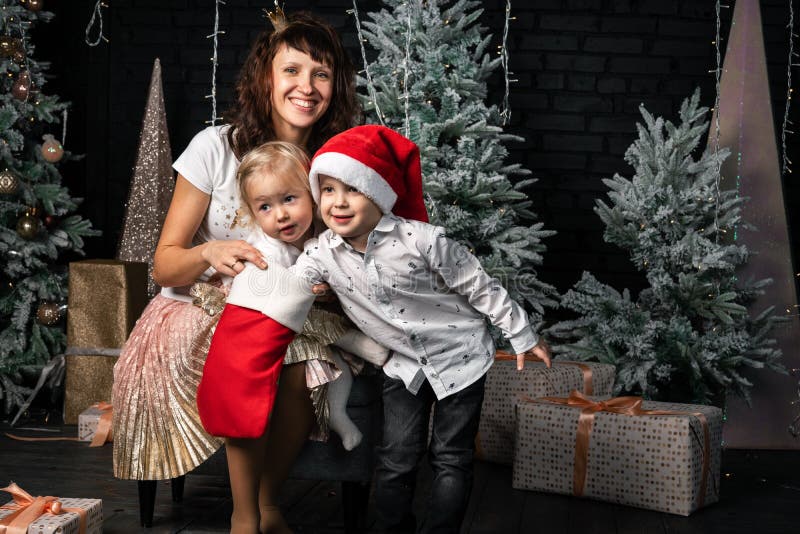 Natale: La mamma in cappuccio di Santa con il suoi figlio e figlia controllerà i regali in un calzino rosso fotografie stock libere da diritti Natale: La mamma in cappuccio di Santa con il suoi figlio e figlia controllerà i regali in un calzino rosso fotografie stock libere da diritti