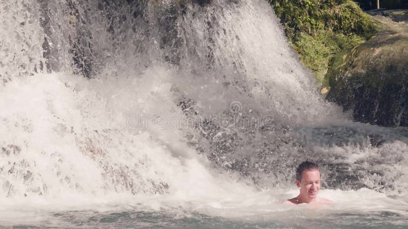 Natation de jeune homme dans l'eau d'éclabousser la cascade dans la jungle tropicale Homme de sourire se baignant en cascade débo