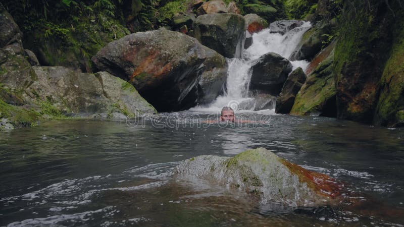 Natation de jeune homme dans le courant de rivière entrant de la cascade dans l'homme de déplacement de forêt tropicale se baigna