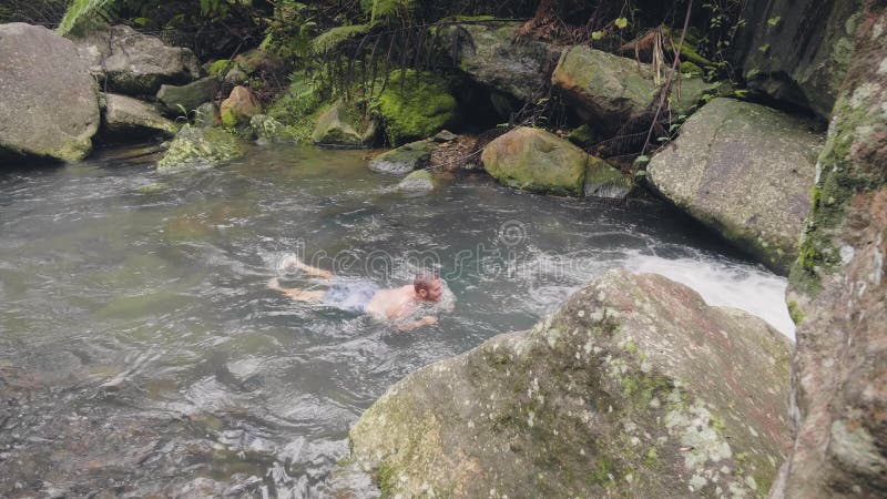 Natation de jeune homme en rivière pierreuse chez l'homme de touristes de forêt tropicale appréciant l'eau douce entrant dans la banque de vidéos