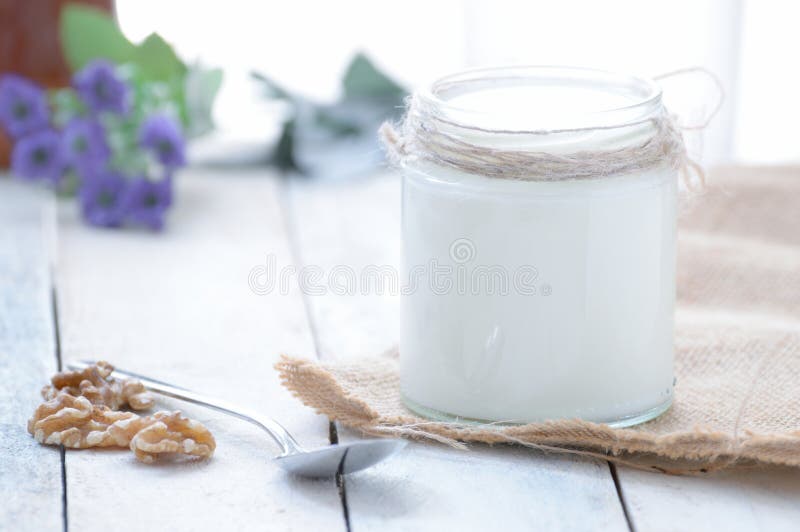 Natural homemade plain yogurt on a burlap fabric next to some nuts and a spoon, served on a white wooden table in a rustic kitchen. Empty copy space.