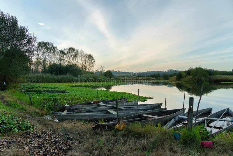 Natural landscape with boats in the water at sunset. Amazing lake with small artisanal fishing boats. Sunrise light reflected in w