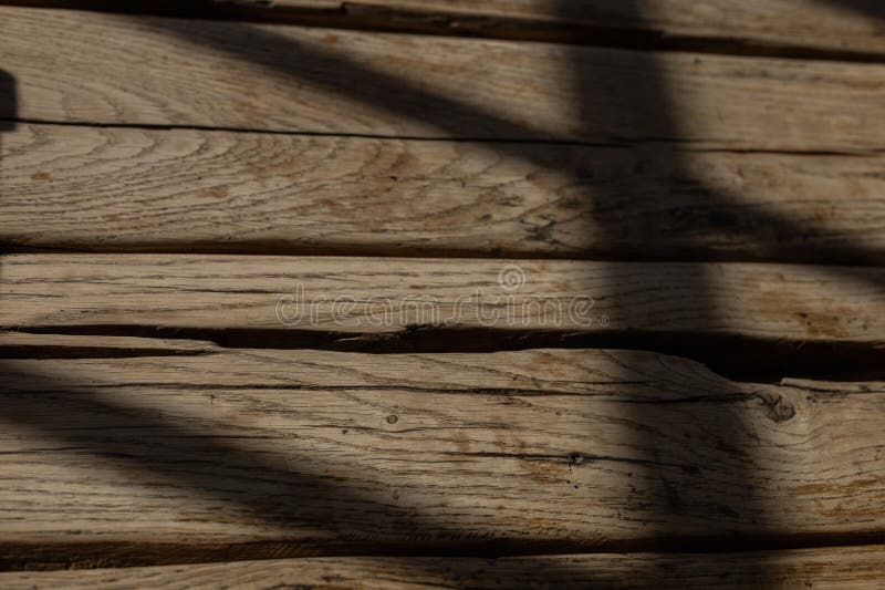 Natural light casting shadows across rustic wooden surface in a cozy indoor setting. Soft, warm light filters through a window, creating an inviting atmosphere in the room. The light forms distinct shadows on the textured surface of a rustic wooden table, showcasing its knots and grains. This tranquil setting reflects a harmonious blend of nature and home, perfect for moments of relaxation or creativity.