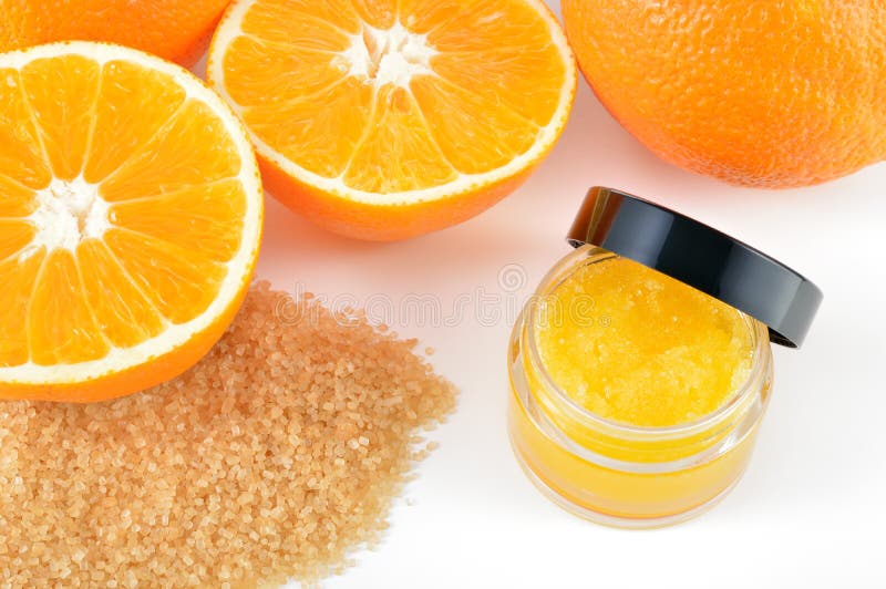 Natural orange sugar lip scrub on white background with reflection. Orange cosmetic in a glass jar with oranges in a background. Natural orange sugar lip scrub on white background with reflection. Orange cosmetic in a glass jar with oranges in a background.