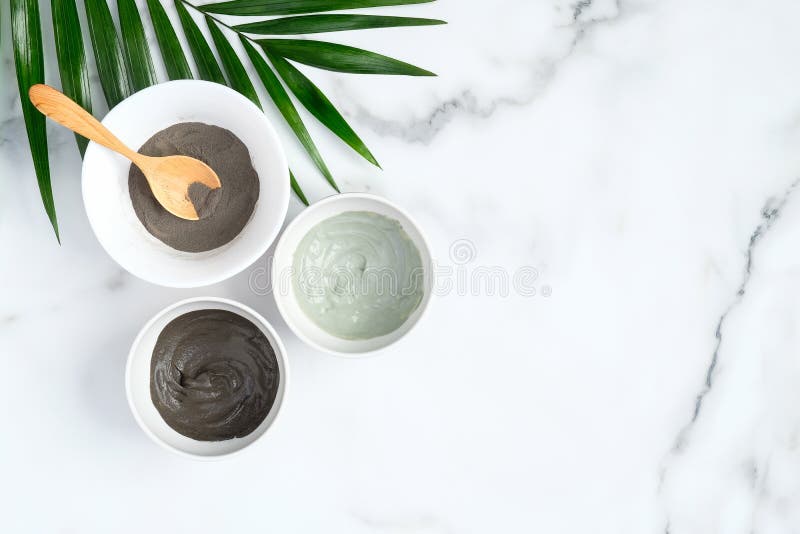 Natural organic SPA clay facial mask in bowls and tropical leaf on marble background. Face skin care and beauty treatment concept