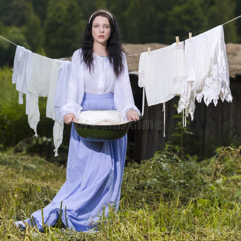 Natural Portrait of Brunette Caucasian Girl With Basin of Laundry Against Hanged Linen on Rope Behind In Countryside