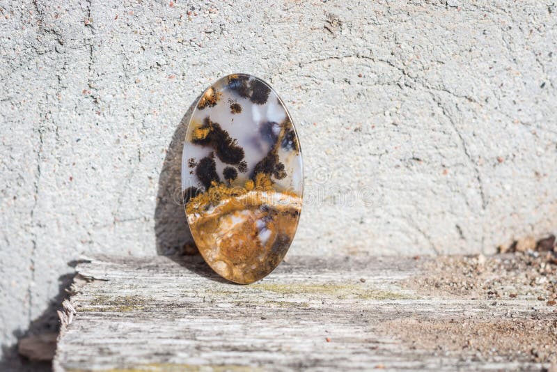 Macro close-up photography of natural gem stone moss agate lying on the wooden surface shelf and with old loft cement background venetian plaster. Macro close-up photography of natural gem stone moss agate lying on the wooden surface shelf and with old loft cement background venetian plaster