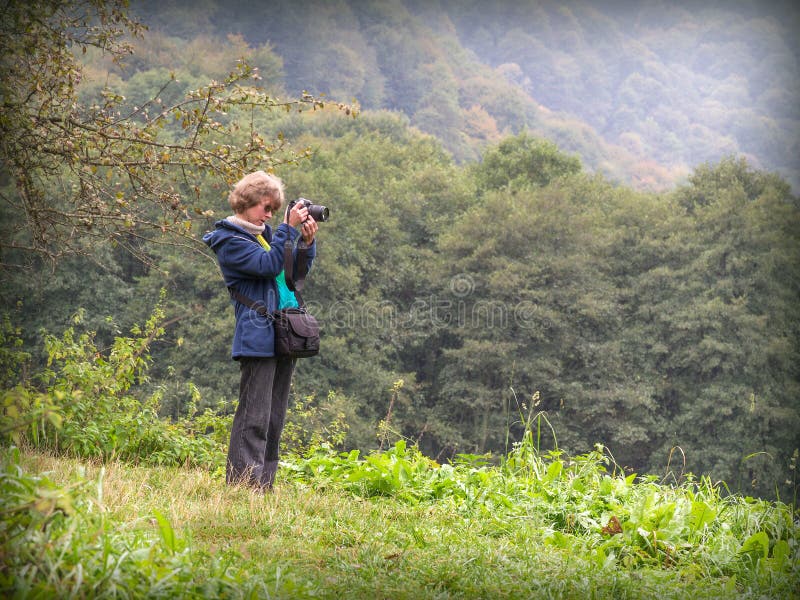 Bello bello blondy caucasica ragazza fotografo stare con la macchina fotografica tra una zona di montagna preparando a sparare un po ' di autunno, natura, scena con foreste, colline e montagne.