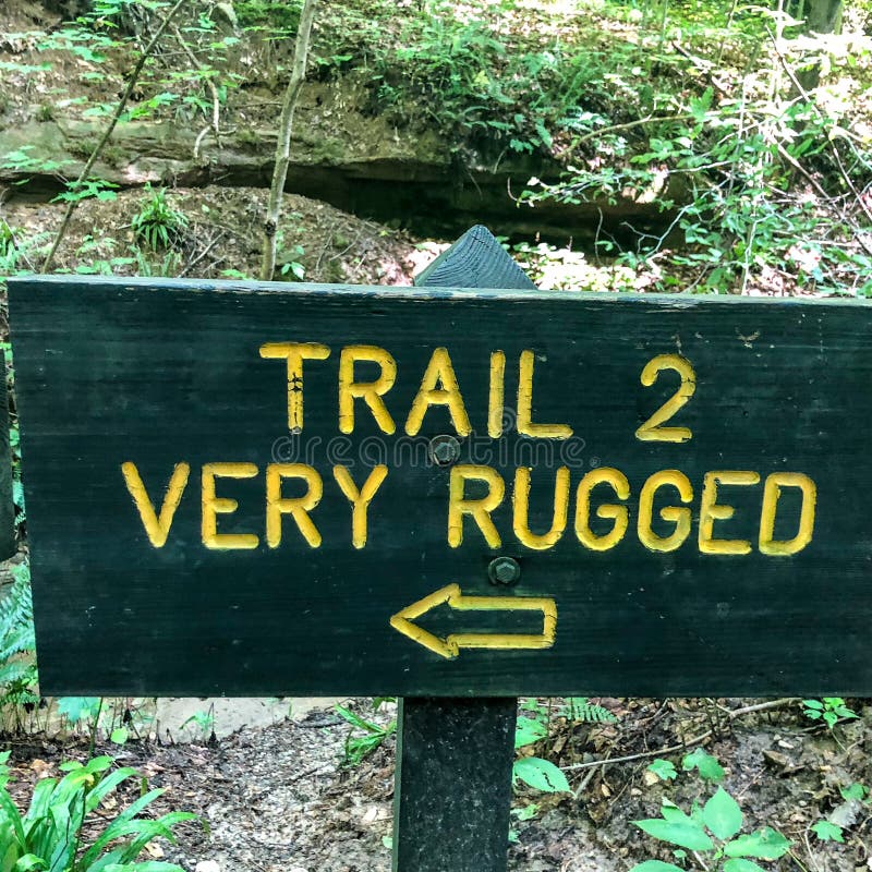 This wooden sign on a nature hiking trail through a state park forest is warning hikers that the terrain ahead is going to be very rugged. This wooden sign on a nature hiking trail through a state park forest is warning hikers that the terrain ahead is going to be very rugged.