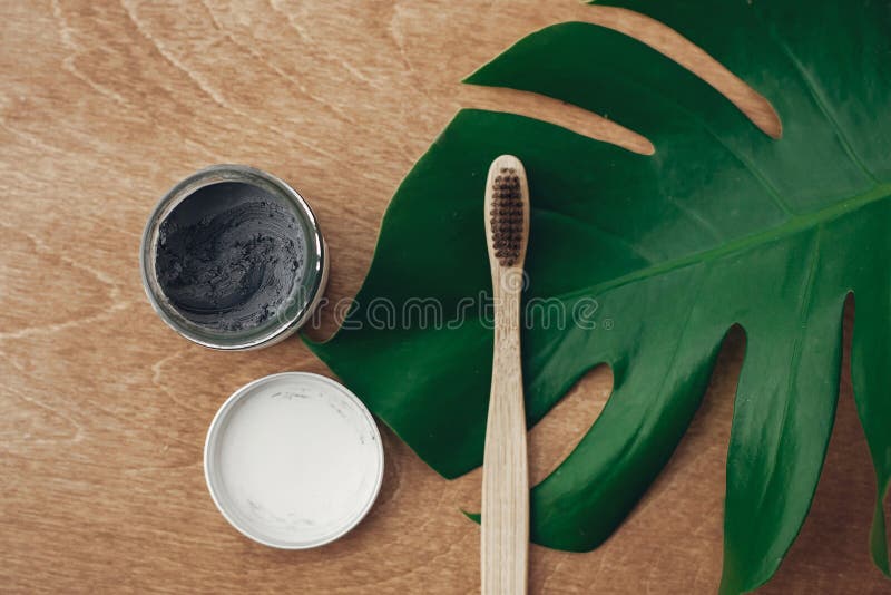 Naturlig tandkräm aktiverade kol- och bambutandborsten på träbakgrund med det gröna monsterabladet Plast- fri skönhet royaltyfri foto