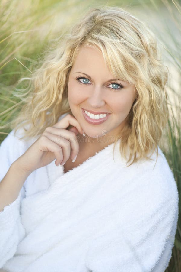 Health and beauty spa concept shot of a beautiful blond haired young woman sitting amongst tall grass and wearing a white toweling bath robe. Health and beauty spa concept shot of a beautiful blond haired young woman sitting amongst tall grass and wearing a white toweling bath robe