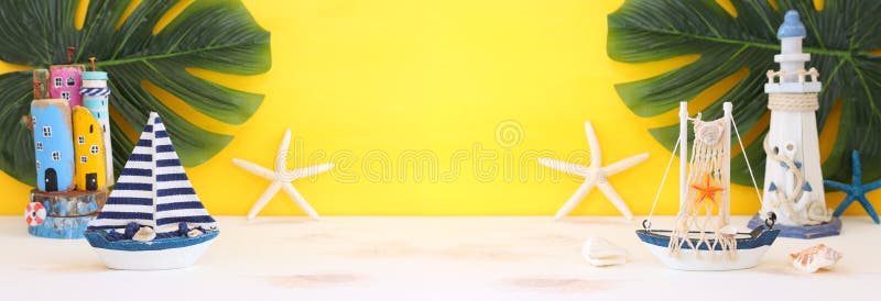 Nautical concept with sea life style objects as boat, driftwood beach houses, seashells and starfish over wooden table and yellow