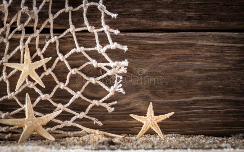 Nautical background with starfish and diamond pattern fishing net on wooden boards with a distinctive woodgrain pattern over fresh beach sand with copyspace. Nautical background with starfish and diamond pattern fishing net on wooden boards with a distinctive woodgrain pattern over fresh beach sand with copyspace