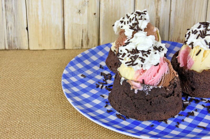 Neapolitan sundae in brown bowl with whipped cream and chocolate sprinkles on blue and white gingham plate on burlap. Neapolitan sundae in brown bowl with whipped cream and chocolate sprinkles on blue and white gingham plate on burlap.